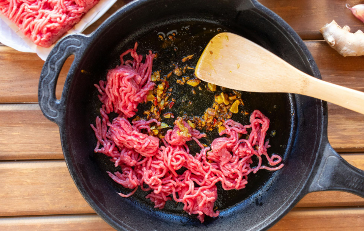 A portion of ground meat being cooked in a cast-iron pan
